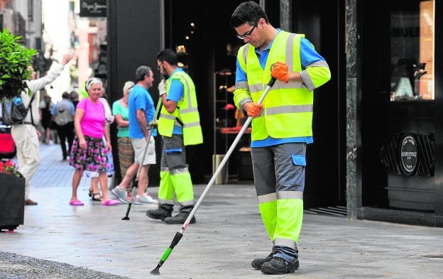 Dos operarios de Ferrovial utilizan sendas rasquetas para eliminar las manchas de chicles en la plaza Esteve Mora.