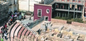 Imagen del graderío y de parte del escenario del Teatro Romano, con el área del antiguo pórtico al fondo, entre matorrales y protegida por la fachada rehabilitada de un viejo edificio. :: ANTONIO GIL / AGM/