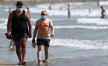 Dos hombres pasean por una playa con mascarilla./Borja Suárez / Reuters