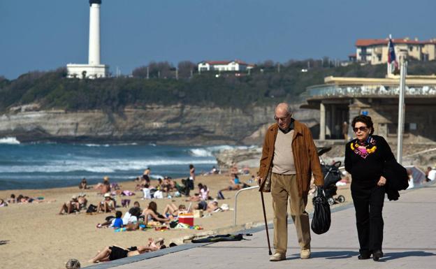 Two retirees stroll along a beach. 