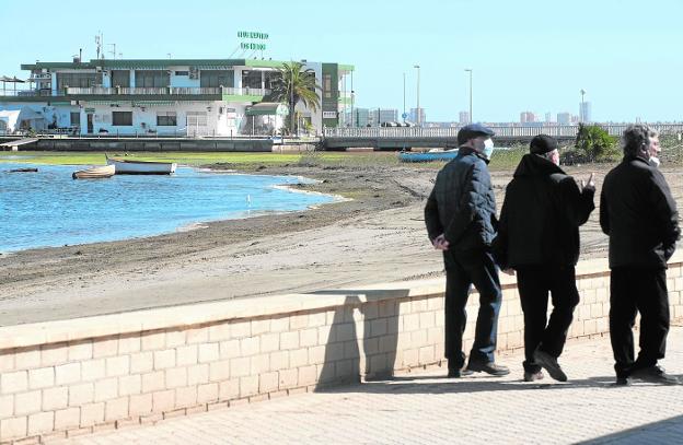 Three neighbors walk along the boardwalk of Los Nietos, yesterday.  In the background, the yacht club surrounded by a green layer in the water. 