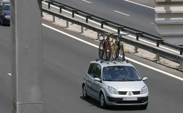 A car drives down the highway with several bicycles on its roof rack. 