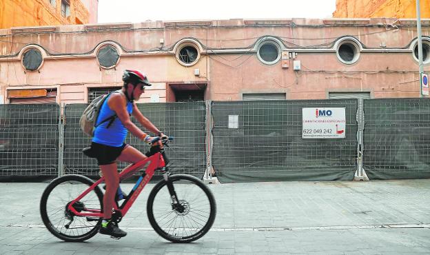 A cyclist crosses the San Agustín square, in front of the fence that delimits the remodeling works of a facade and construction of a residential building. 