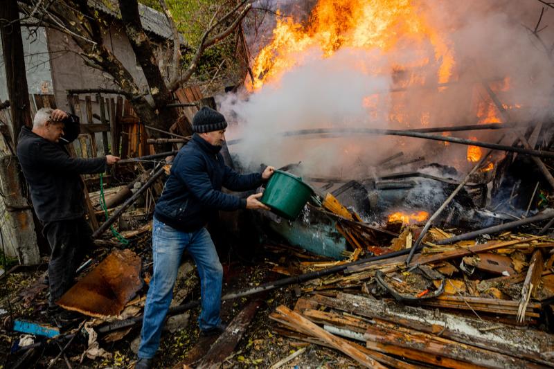 Two residents of Bakhmut try to put out the flames that devour the remains of their house bombed by the Russians